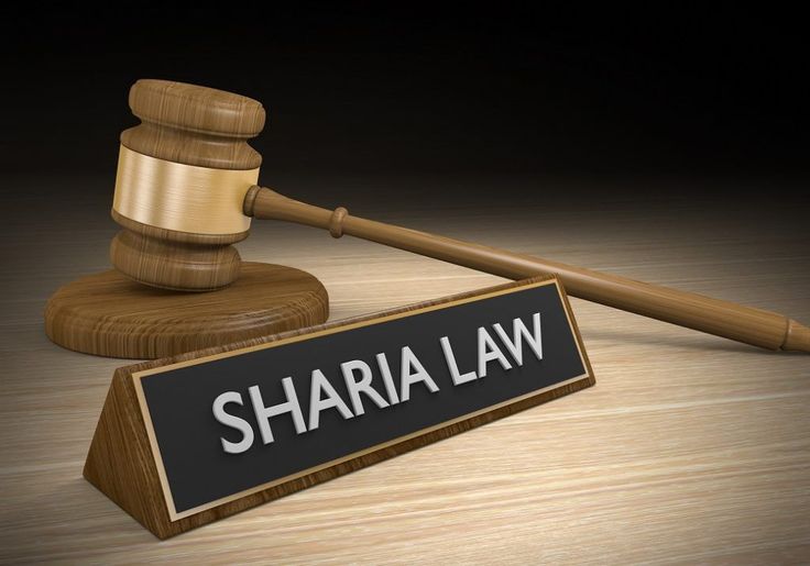 A wooden board on which Sharia Law is written with a hammer behind it.